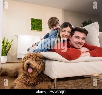 Famille souriante allongée sur le canapé près du chien à la maison Banque D'Images