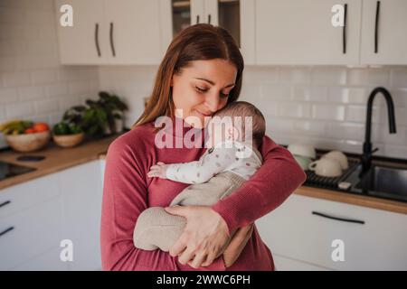 Femme souriante embrassant bébé fille dans la cuisine Banque D'Images