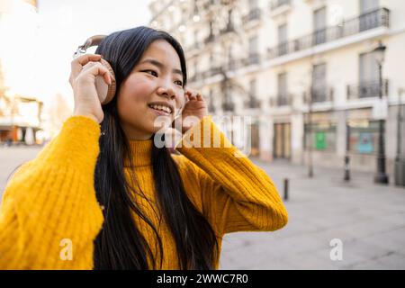 Heureuse jeune femme portant des écouteurs sans fil près du bâtiment Banque D'Images