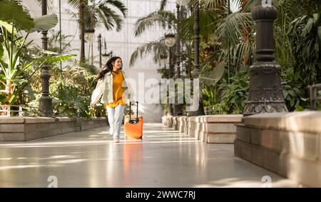 Femme heureuse marchant avec une valise près des plantes Banque D'Images