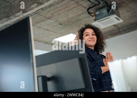 Femme d'affaires souriante debout avec les mains serrées près de l'ordinateur dans le bureau Banque D'Images