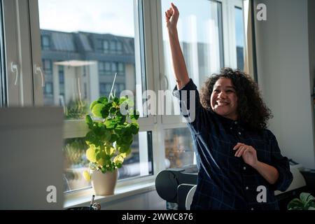 Femme réussie levant la main et célébrant près de la fenêtre dans le bureau Banque D'Images