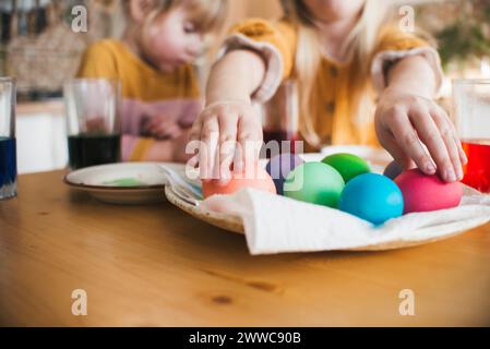 Fille arrangeant des oeufs de Pâques colorés dans une assiette sur la table à la maison Banque D'Images