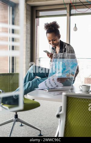 Jeune femme d'affaires avec téléphone intelligent examinant le document dans le bureau Banque D'Images