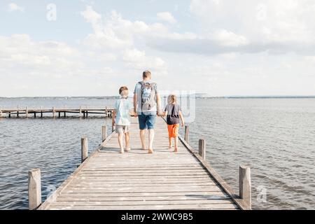 Père marchant avec ses fils sur la jetée en bois au lac Banque D'Images