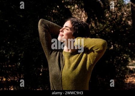 Femme souriante debout avec les mains derrière la tête au parc Banque D'Images