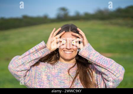 Femme souriante couvrant les yeux de fleurs Banque D'Images