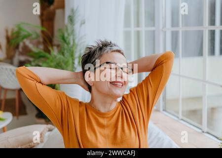 Femme heureuse avec les yeux fermés et les mains derrière la tête à la maison Banque D'Images