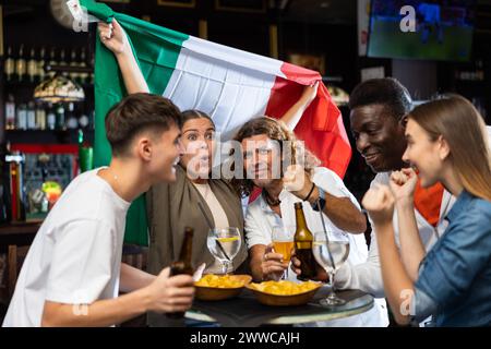 Les fans de football internationaux agitent le drapeau italien et soutiennent l'équipe nationale dans le bar des sports Banque D'Images