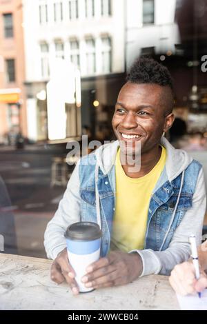 Homme souriant regardant par la fenêtre assis dans le café Banque D'Images