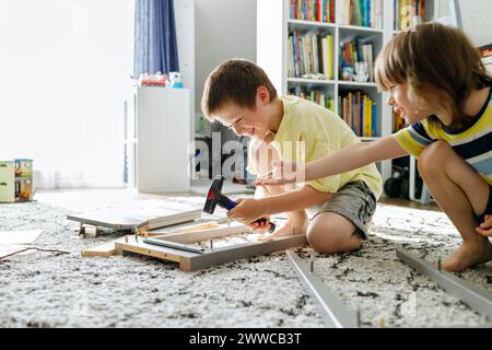 Frères ludiques apprenant à assembler une table de chevet à la maison Banque D'Images