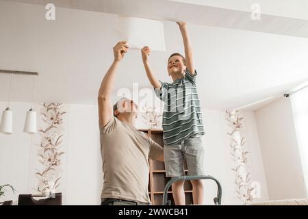 Heureux garçon et père pelant vieux papier peint du plafond à la maison Banque D'Images