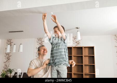 Fils heureux aidant le père à peler le vieux papier peint du plafond à la maison Banque D'Images