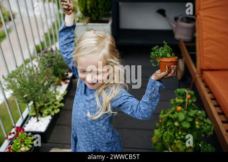 Jeune fille joyeuse tenant la plante dans le jardin du balcon Banque D'Images