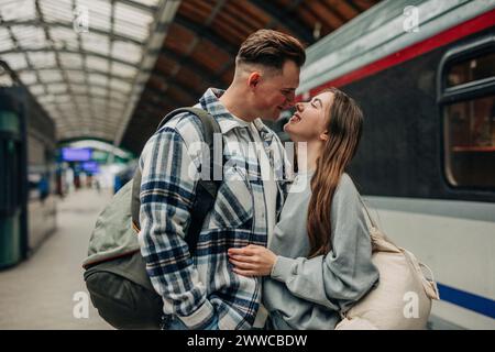 Couple aimant debout avec des sacs à dos à la gare Banque D'Images