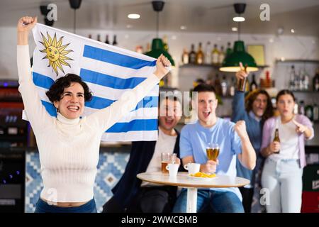 Criant de jeunes fans de sport adultes qui se sont pris pour l'équipe préférée et qui ont gagné le drapeau de l'Uruguay tout en regardant le match ensemble au pub Banque D'Images