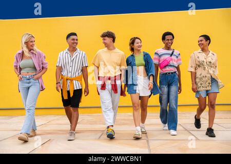 Groupe multi-ethnique de jeunes amis marchant côté seide devant le mur jaune Banque D'Images