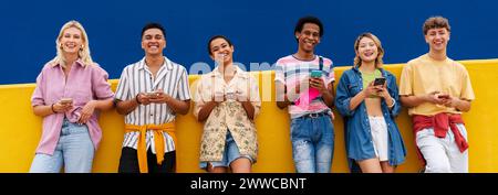 Groupe d'amis s'appuyant contre le mur jaune à l'aide de leurs smartphones Banque D'Images