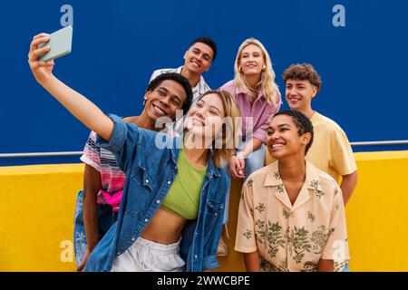 Groupe d'amis amis avec des vêtements colorés assis sur le mur jaune prenant la photo de groupe Banque D'Images