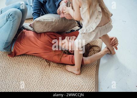 Mère et père joyeux jouant avec leur fille sur tapis à la maison Banque D'Images