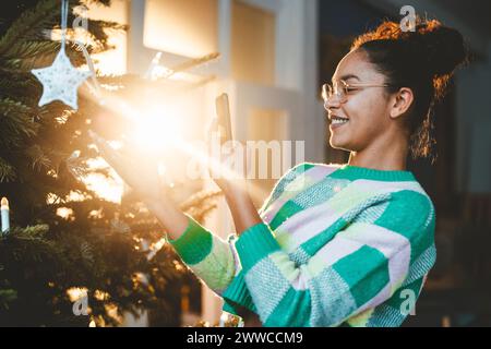 Jeune femme photographiant l'arbre de Noël au-dessus d'un téléphone intelligent Banque D'Images