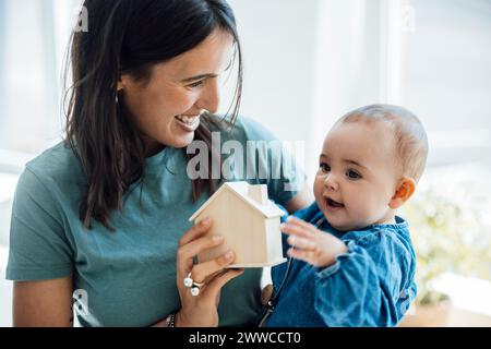 Heureuse mère montrant la maison modèle en bois à la petite fille Banque D'Images