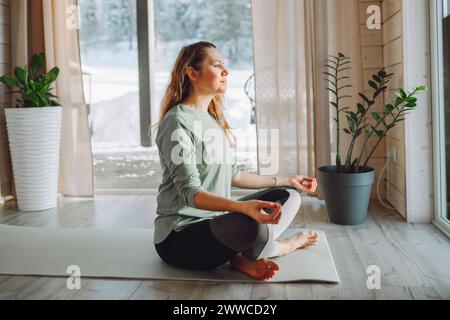 Femme assise dans la pose de yoga lotus à la maison Banque D'Images