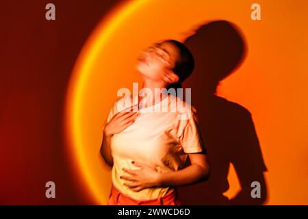 Jeune femme dans l'éclairage au néon sur fond orange Banque D'Images