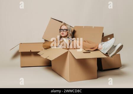 Femme d'affaires assise dans la boîte de carton sur fond blanc Banque D'Images