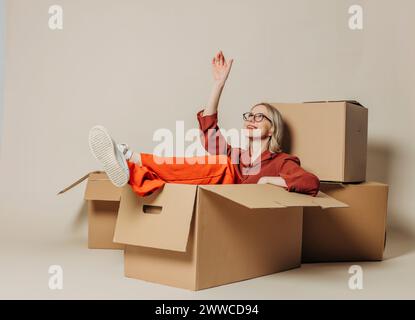 Femme d'affaires souriante assise dans la boîte de carton et le jour rêvant sur fond blanc Banque D'Images