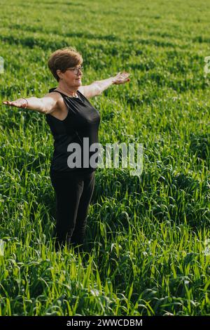 Femme âgée exerçant avec les bras tendus dans la prairie Banque D'Images