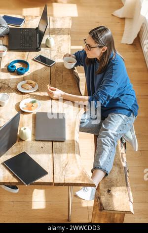 Technicien INFORMATIQUE assis avec du thé et des biscuits à table dans le bureau de démarrage Banque D'Images