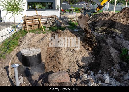 Utilisation d'une excavatrice pour enterrer une fosse septique en béton de 10 m3 située dans le jardin à côté de la maison. Banque D'Images