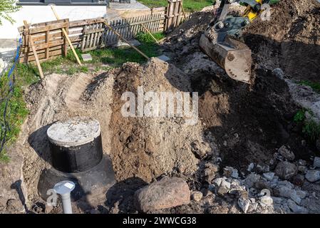 Utilisation d'une excavatrice pour enterrer une fosse septique en béton de 10 m3 située dans le jardin à côté de la maison. Banque D'Images