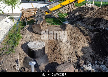 Utilisation d'une excavatrice pour enterrer une fosse septique en béton de 10 m3 située dans le jardin à côté de la maison. Banque D'Images