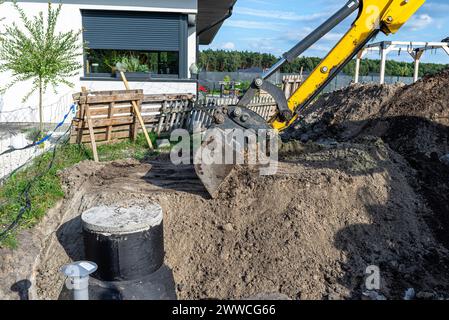 Utilisation d'une excavatrice pour enterrer une fosse septique en béton de 10 m3 située dans le jardin à côté de la maison. Banque D'Images