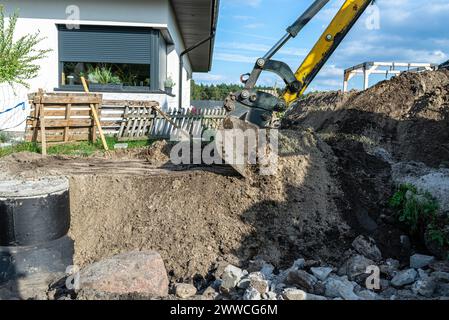 Utilisation d'une excavatrice pour enterrer une fosse septique en béton de 10 m3 située dans le jardin à côté de la maison. Banque D'Images