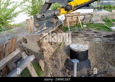 Utilisation d'une excavatrice pour enterrer une fosse septique en béton de 10 m3 située dans le jardin à côté de la maison. Banque D'Images