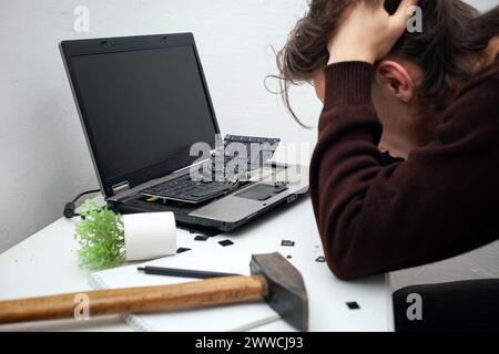 L'homme a détruit l'ordinateur portable avec un marteau. Travail nerveux, ordinateur buggy, erreurs, Internet lent, non sauvegardé dans le jeu, texte imprimé, accroché. Mauvais vieux comput Banque D'Images