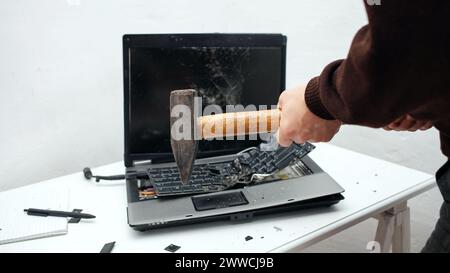 L'homme a détruit l'ordinateur portable avec un marteau. Travail nerveux, ordinateur buggy, erreurs, Internet lent, non sauvegardé dans le jeu, texte imprimé, accroché. Mauvais vieux comput Banque D'Images