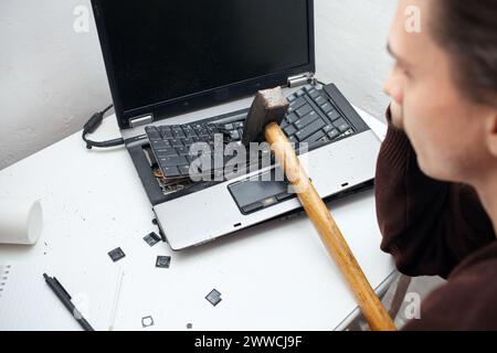 L'homme a détruit l'ordinateur portable avec un marteau. Travail nerveux, ordinateur buggy, erreurs, Internet lent, non sauvegardé dans le jeu, texte imprimé, accroché. Mauvais vieux comput Banque D'Images