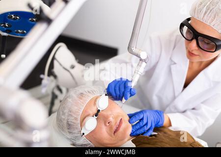 Cosmétologue en train de réaliser la procédure d'enlèvement de mole laser pour la femme âgée Banque D'Images