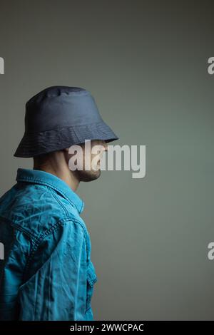 Un jeune modèle masculin élégant avec une barbe bien soignée portant une chemise bleue et un chapeau sombre, posant en toute confiance pour l'appareil photo. Banque D'Images