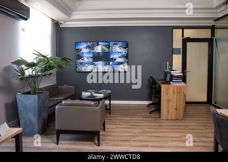 Un intérieur de bureau élégant et moderne avec des murs gris foncé, une grande fenêtre et un moniteur sur le mur. meubles confortables en cuir. Banque D'Images