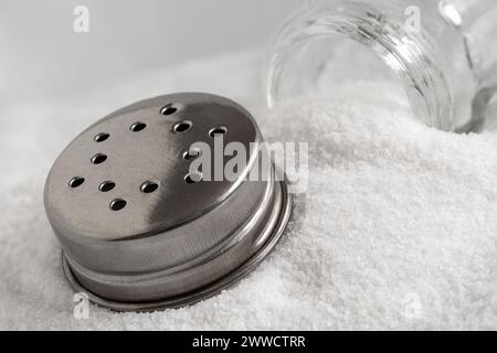 Salière en verre et couvercle en métal reposant sur le sel de mer. Banque D'Images