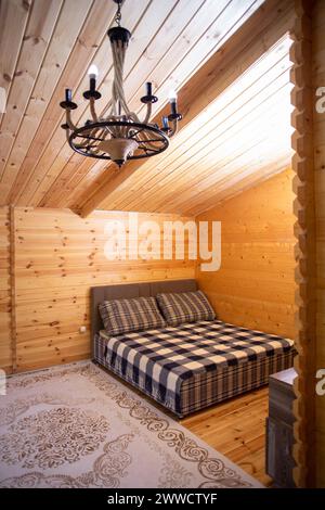 La chambre est décorée avec des lambris de bois chaleureux et un lit doux et accueillant. Un beau lustre fournit un éclairage doux. Banque D'Images