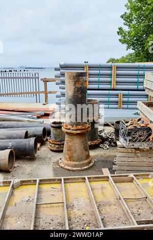 Grand tuyau de fer à l'extrémité à côté de la pile de tubes en PVC Banque D'Images