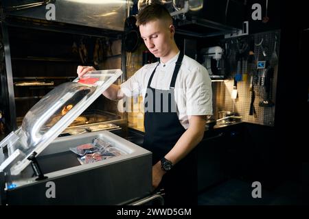 Jeune homme de chef caucasien mettant la viande sous vide dans le réfrigérateur pour le stockage Banque D'Images