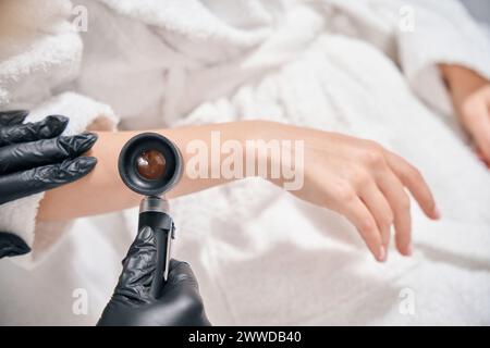 Vue partielle de dessus de l'esthéticienne examinant la peau de la main avec dermatoscope de la femme Banque D'Images