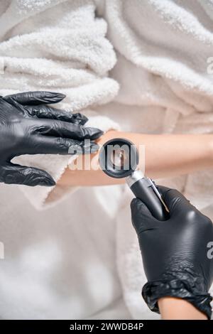 Vue de dessus rognée de cosmétologue examinant la peau de la main avec dermatoscope de la femme Banque D'Images